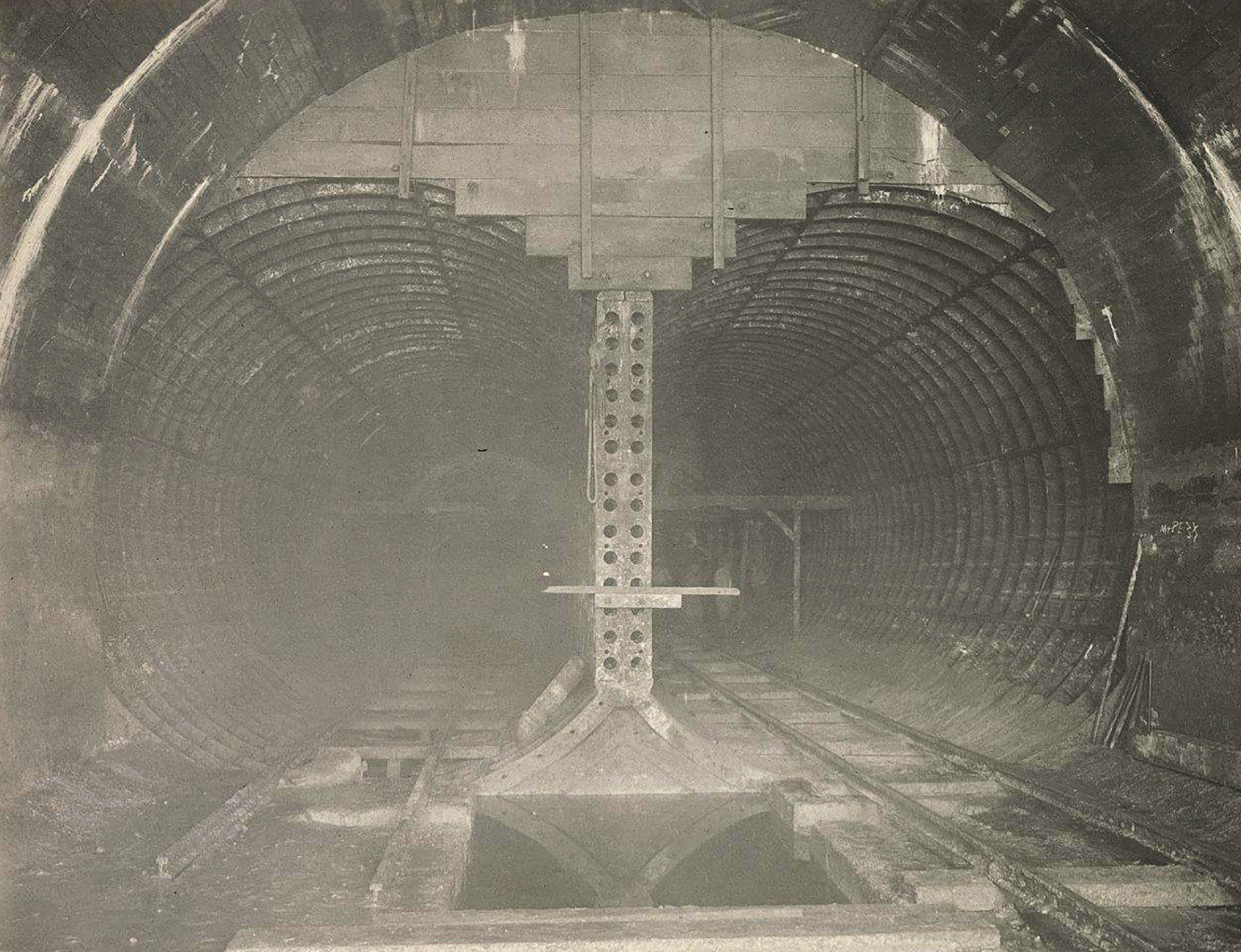 Photograph shows the interior of a subway tunnel with its parallel steel tubes and tracks.