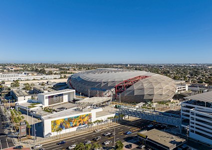 A sports arena sits amid the cityscape. There are walkways to the arena and many open entertainment and gathering spaces in front of the stadium. 
