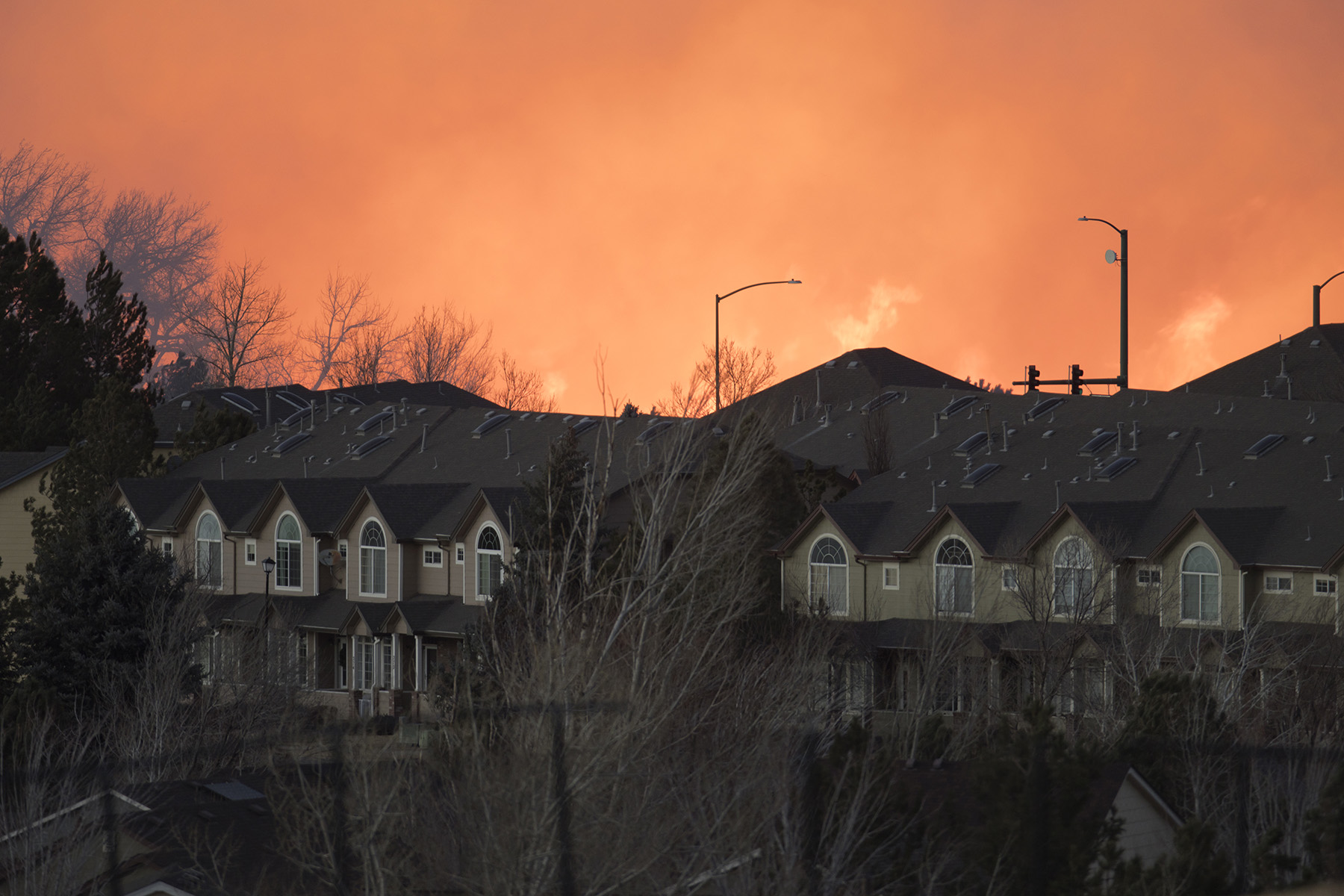 In the foreground are intact homes. In the background, the sky is hazy because of wildfire in the distance.