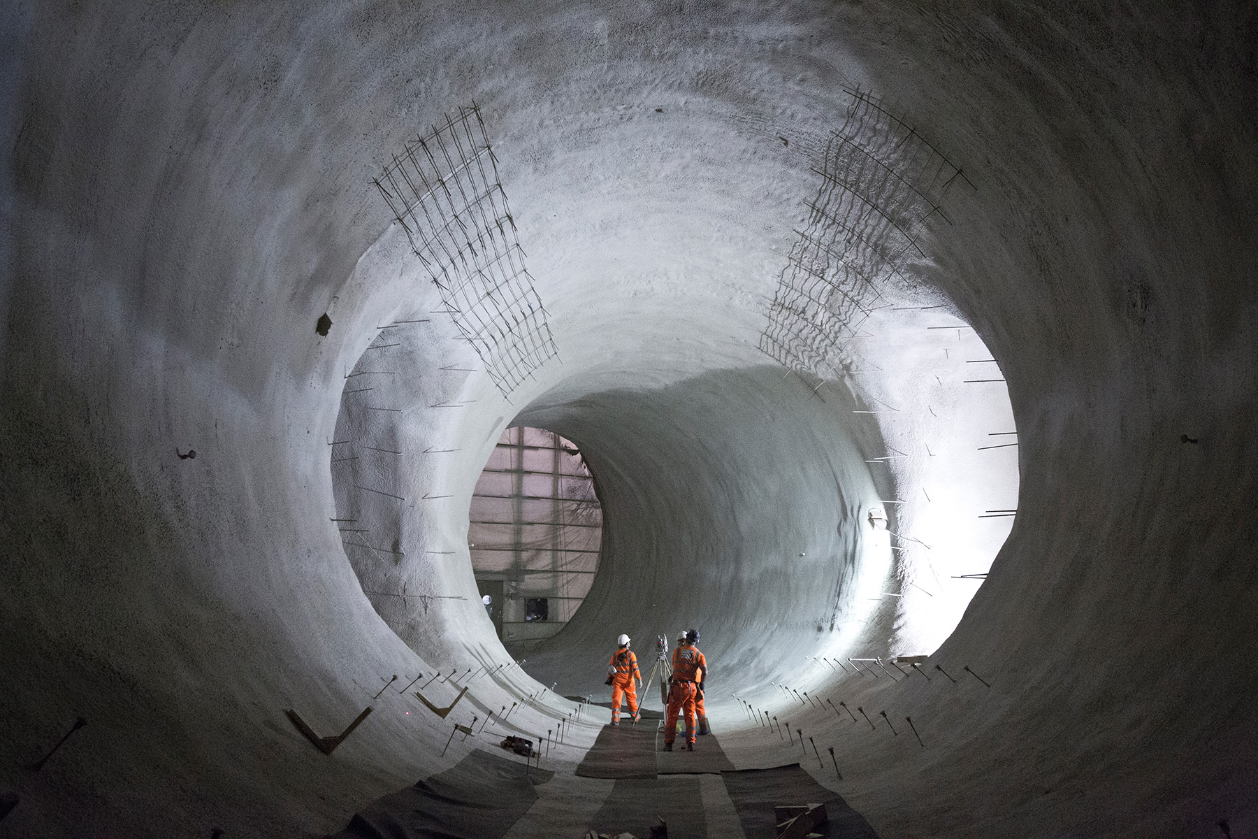 Three men in orange stand inside a giant concrete space with adjoining tunnels.