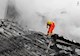 A first responder in full orange personal protective gear and thick goggles stands on a mound of collapsed structure. 