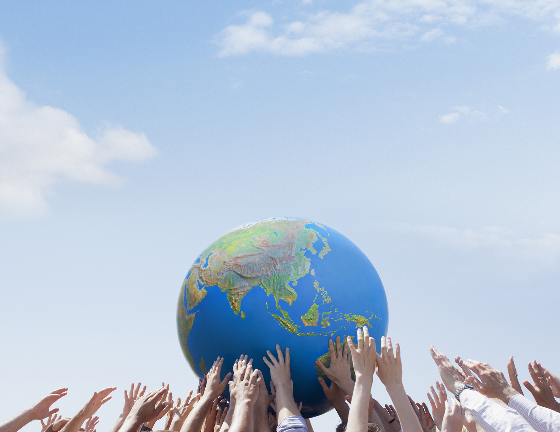 Hands hold up a ball that has the continents on it.